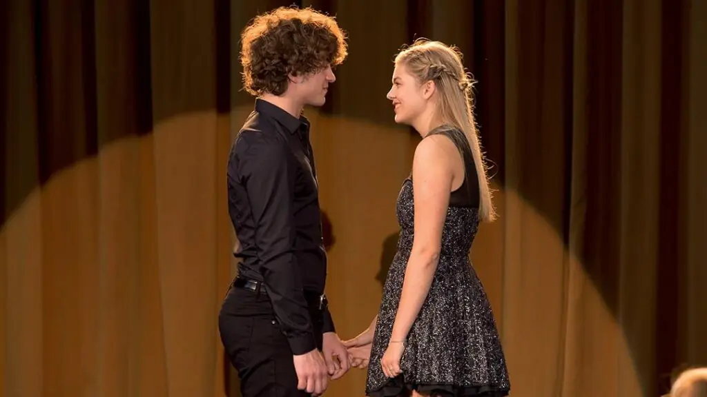 Still from La Famille Bélier, a young man and woman staring into each other's eyes on stage during their singing performance.