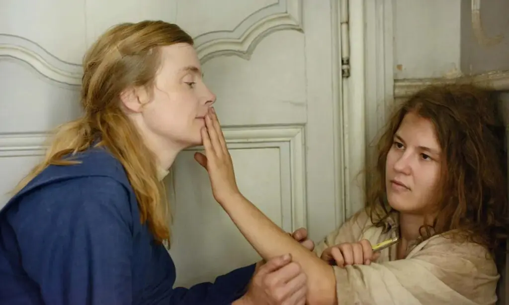 Still from Marie Heurtin: a sighted nun sits on the floor with a deafblind girl who traces her face with her fingers.