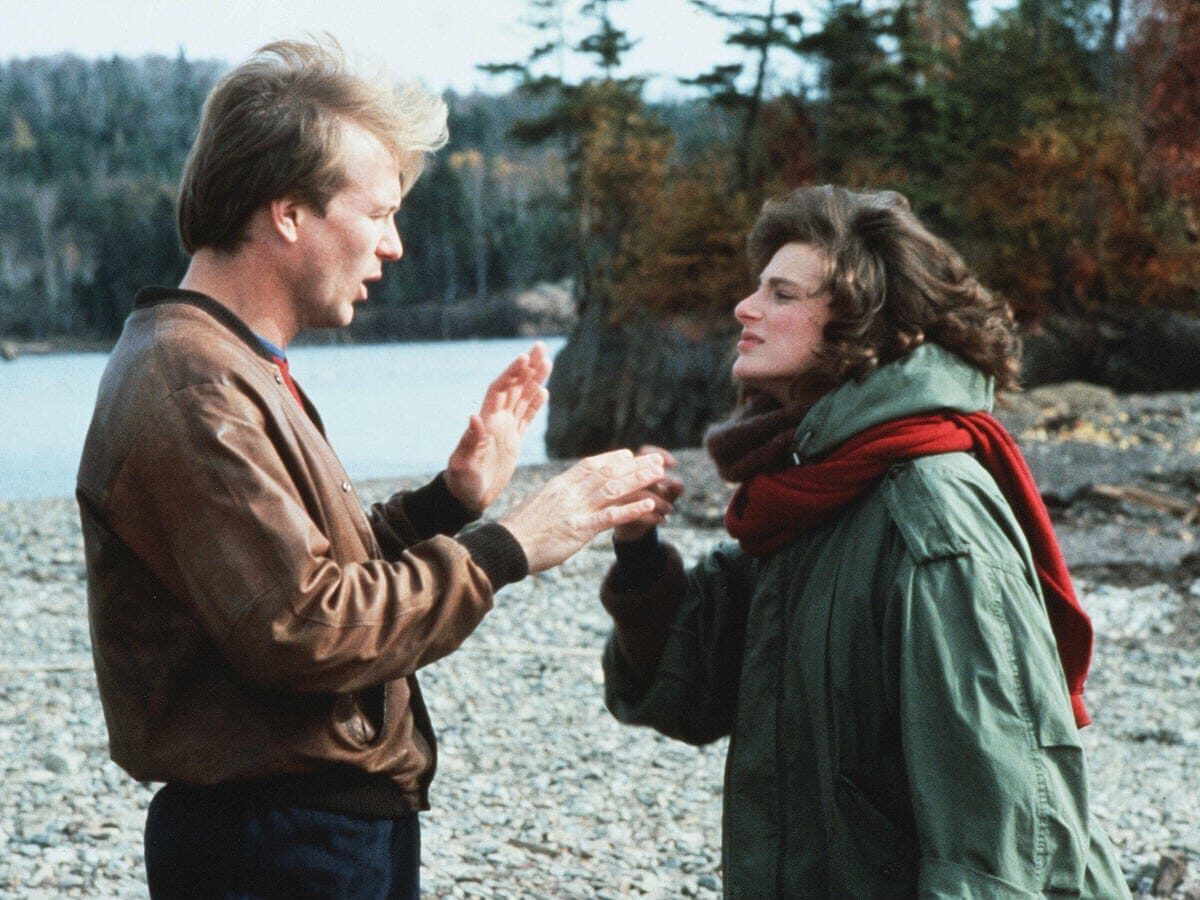 Still from the film Children of a Lesser God, showing a man and woman arguing in sign language on the shores of a lake