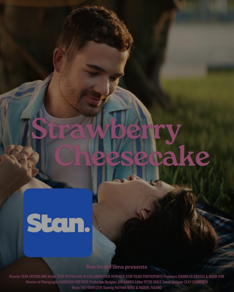 Film poster of a white man and woman lying in grass and smiling at each other. The film's title, Strawberry Cheesecake, is overlaid in pink text. The Stan streaming logo is in the bottom left corner.