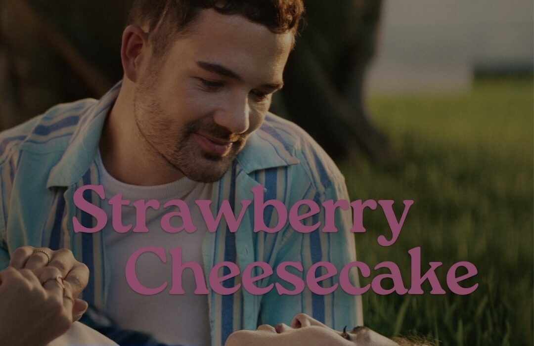 Film poster of a white man and woman lying in grass and smiling at each other. The film's title, Strawberry Cheesecake, is overlaid in pink text. The Stan streaming logo is in the bottom left corner.