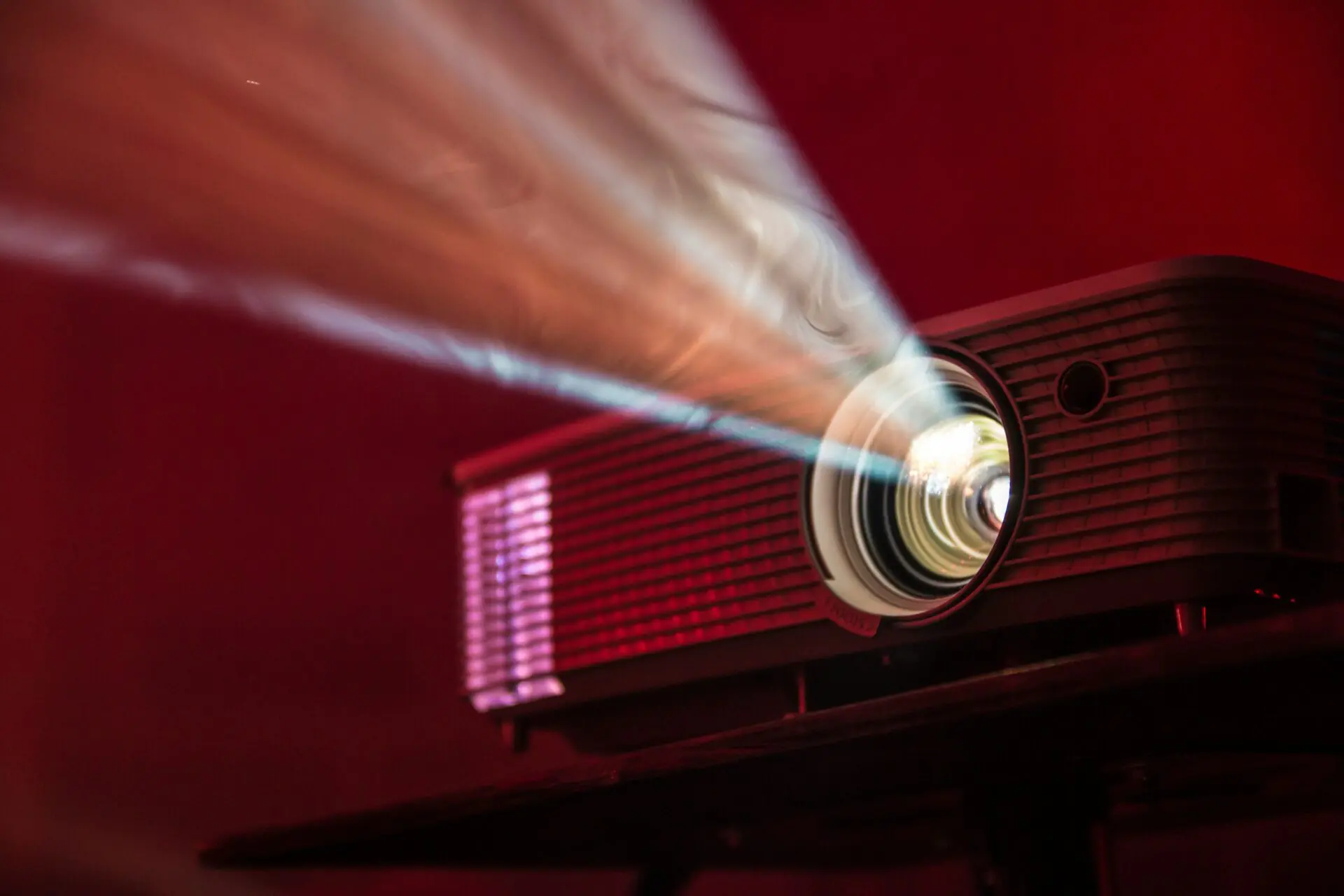 Screen projector with beam of coloured light against dark room