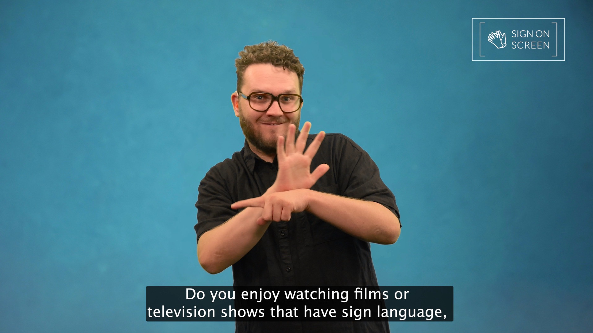 Man with glasses and beard signs in Auslan against blue screen