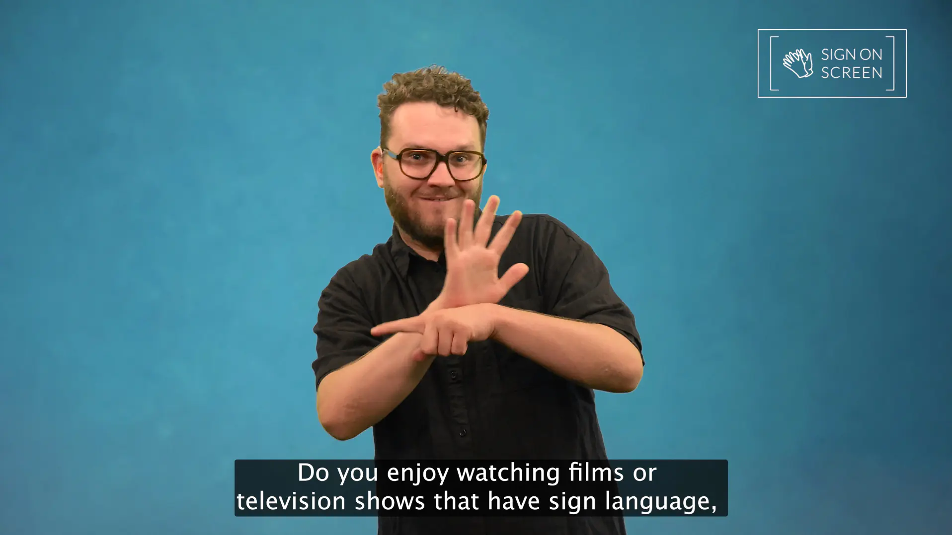 Man with glasses and beard signs in Auslan against blue screen