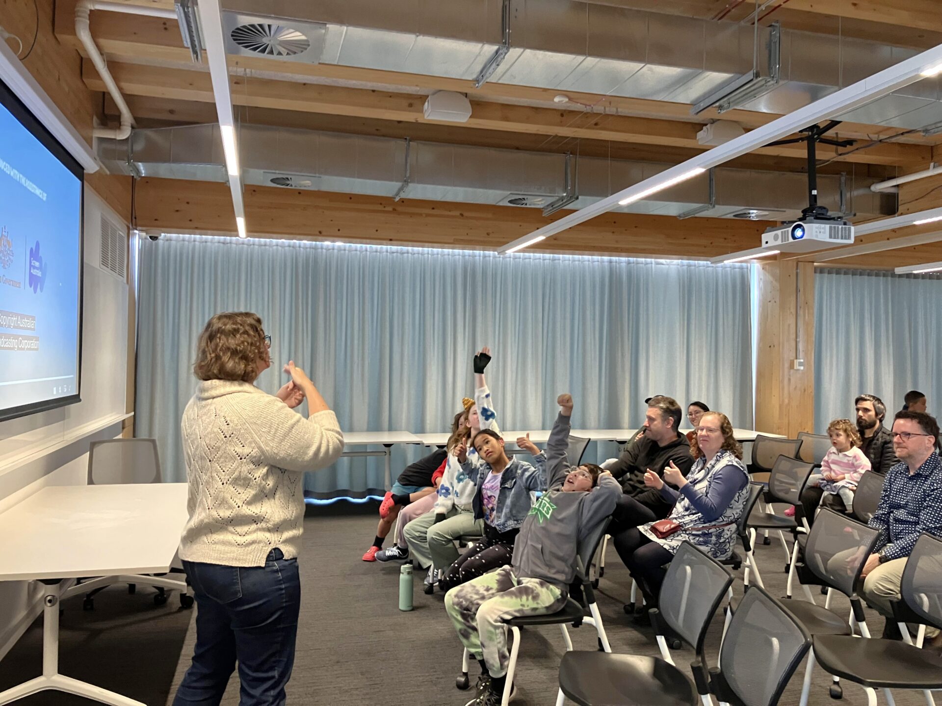 Woman signs to seated children in front of a projector screen