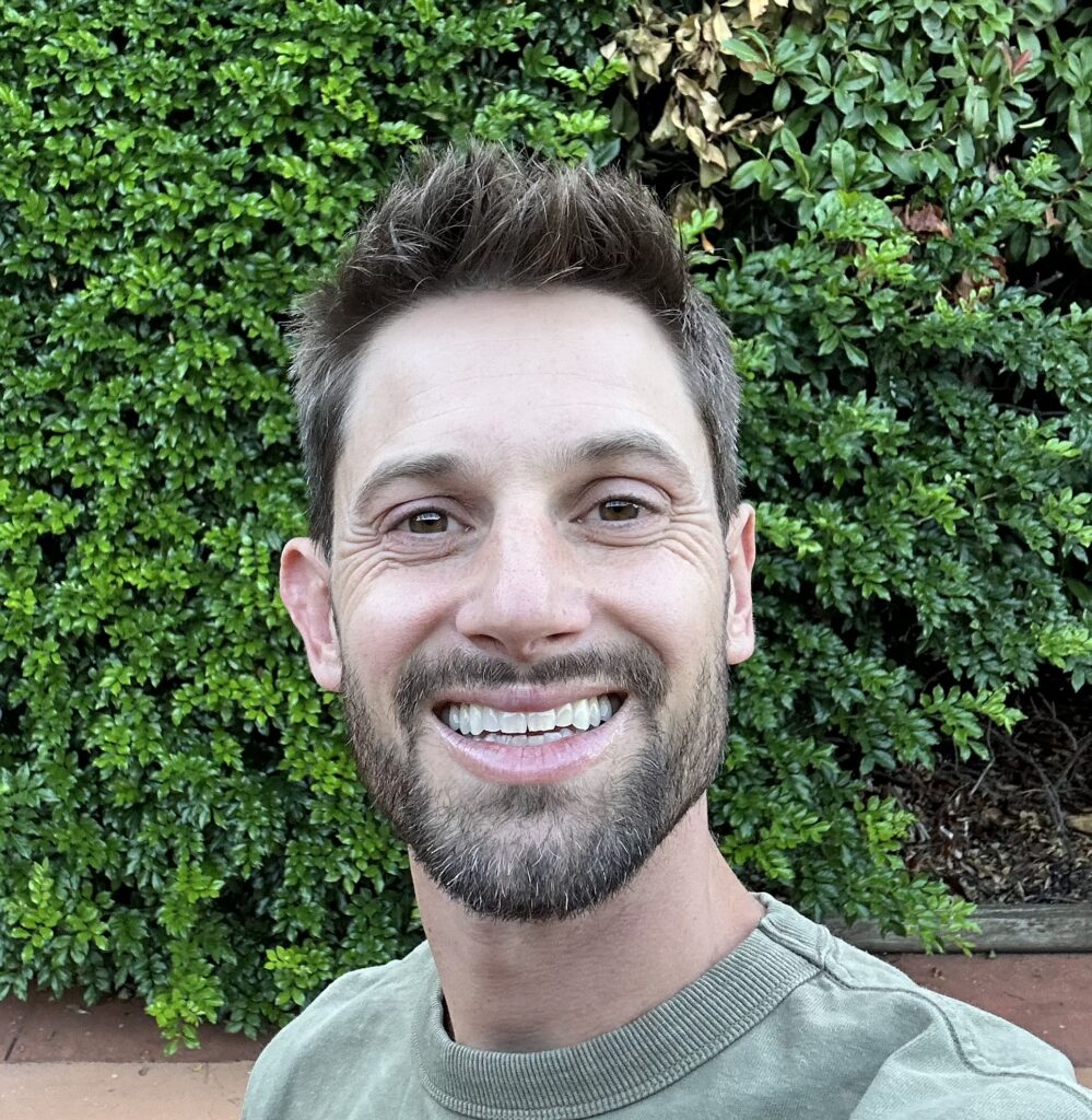 Bearded man smiles against a leafy background