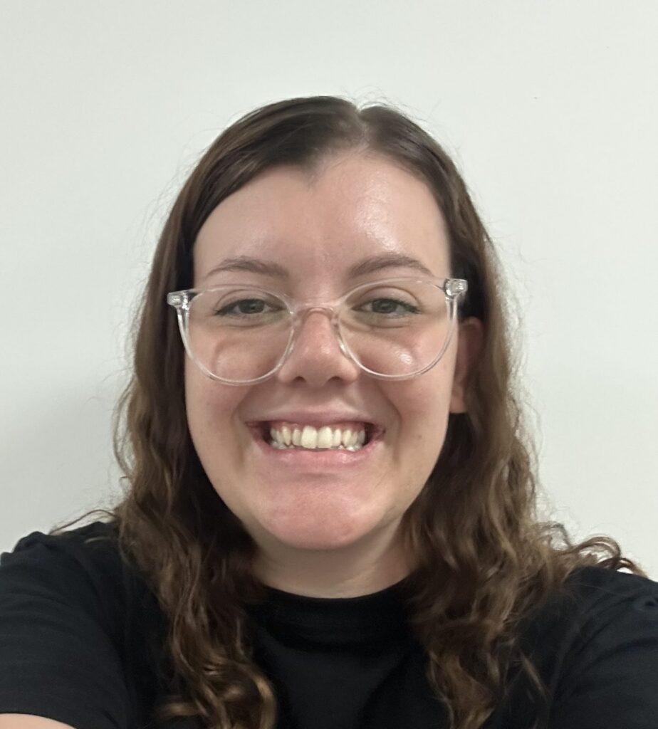 Woman with curly hair and glasses smiles against a grey background