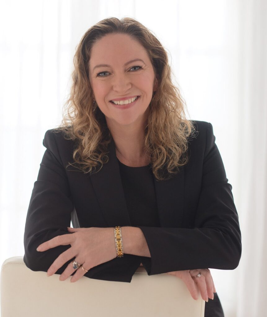 Woman with light hair in black suit smiles against a light background