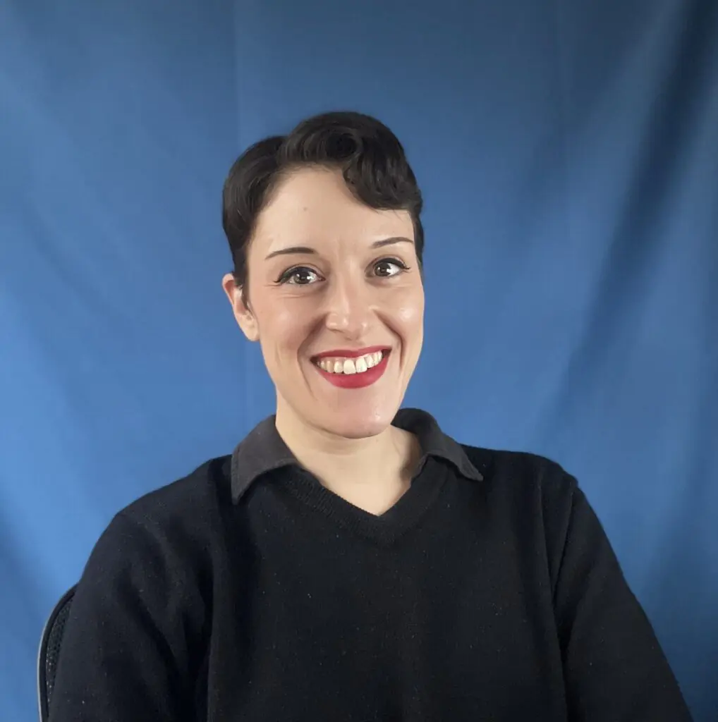 Woman with short, black hair smiles against blue background