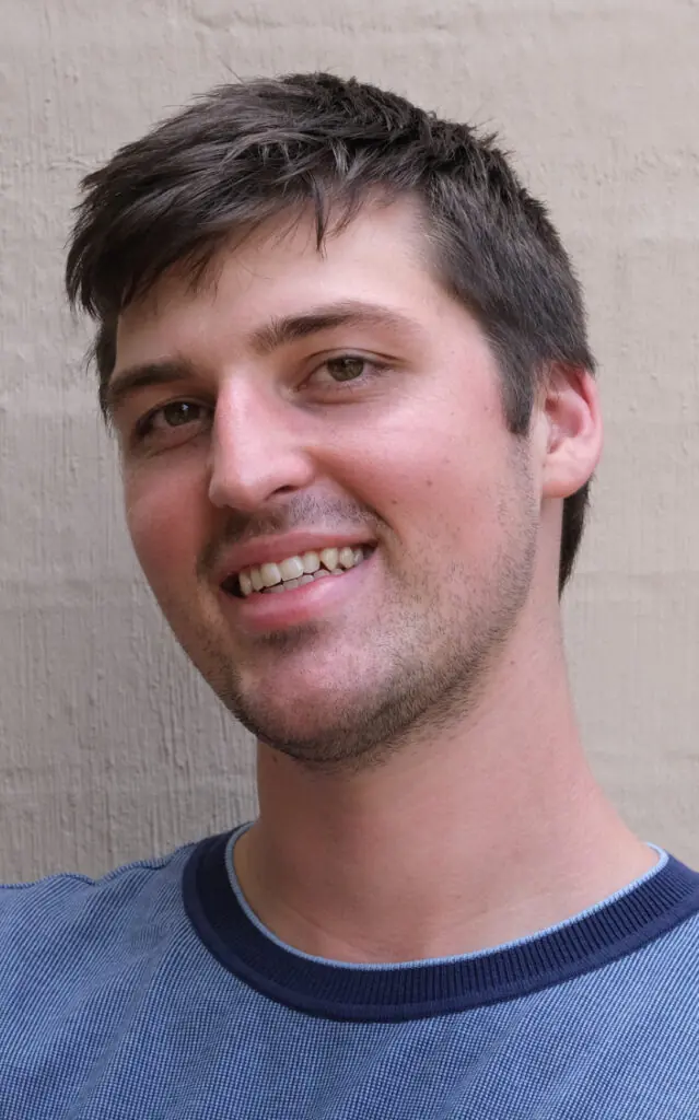 Man with short brown hair in blue top smiles against a grey background
