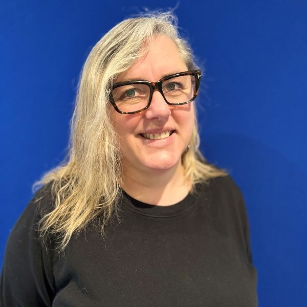 Blonde woman with glasses smiles against blue background