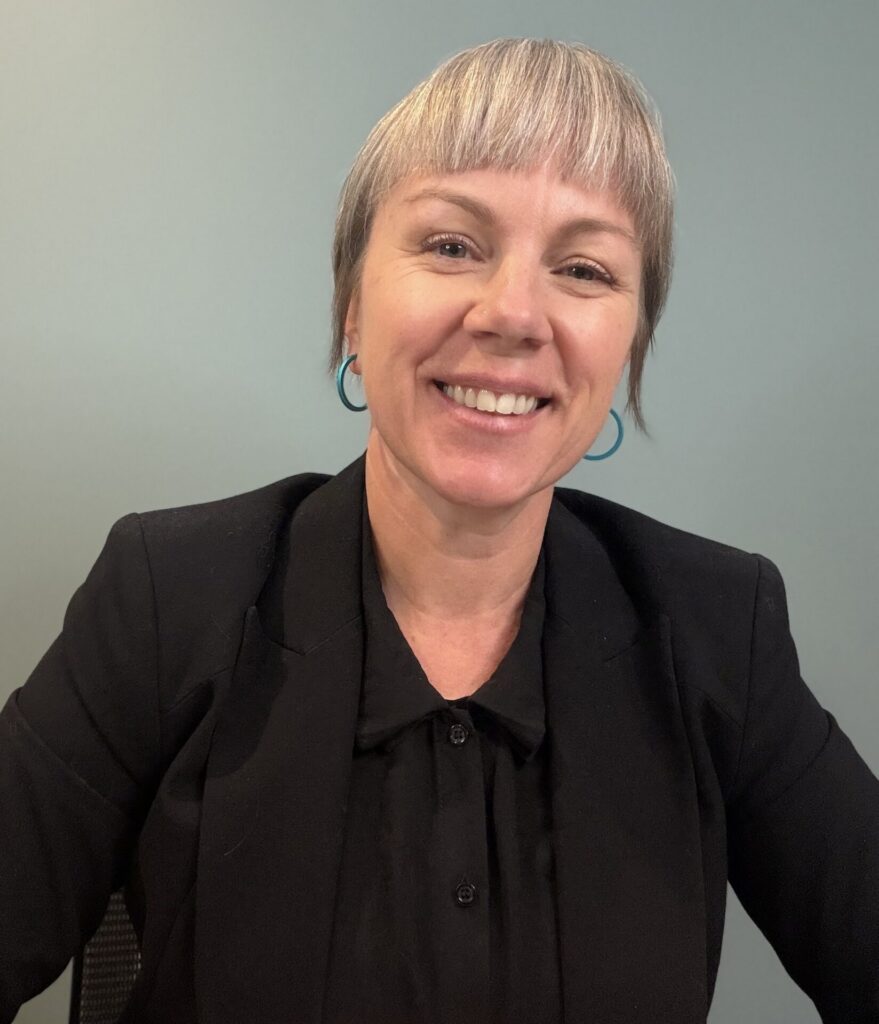 Blonde woman with fringe smiles against grey background