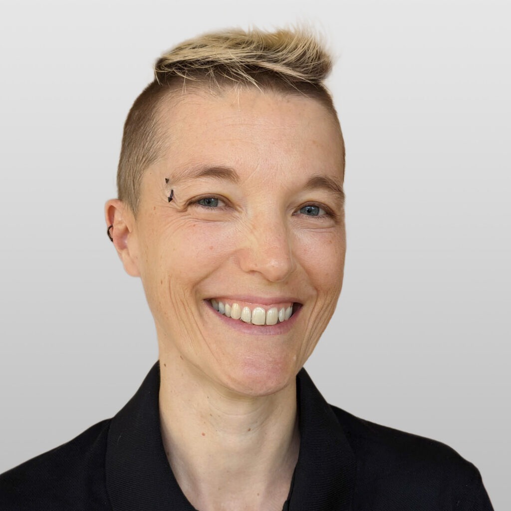 Short-haired blond person smiles against white background