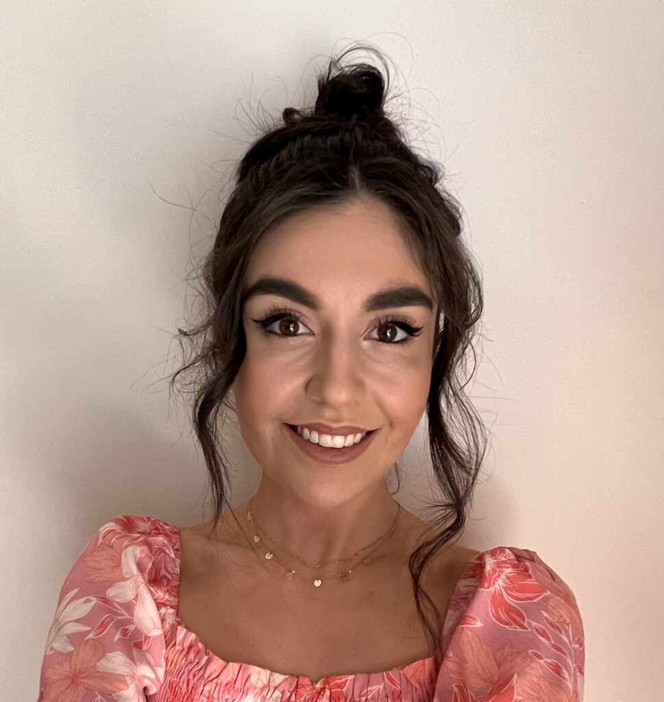 Dark-haired woman in pink dress smiles against cream background
